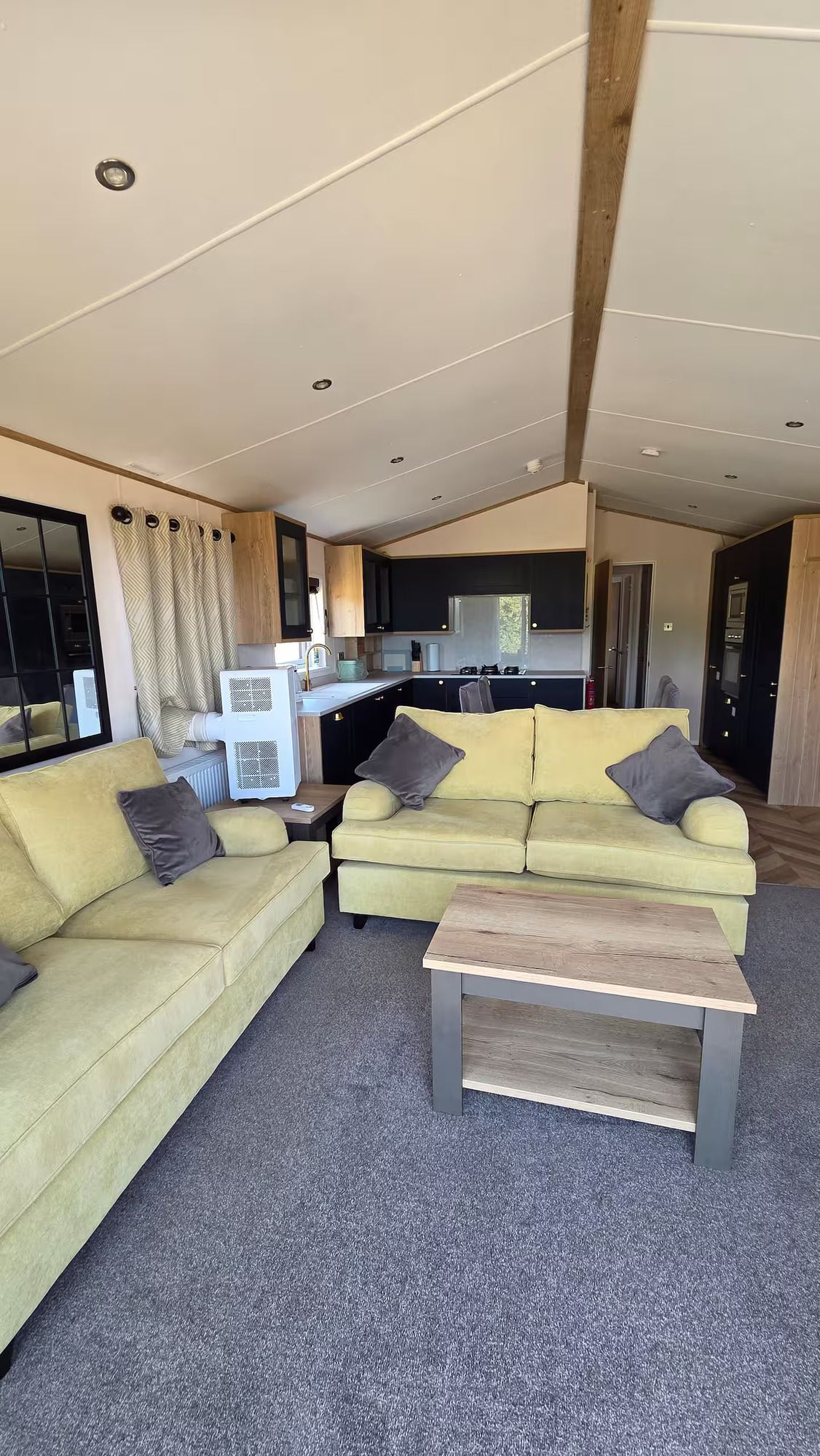 Modern living room with green sofas, coffee table, carpet, and vaulted ceiling with exposed beam