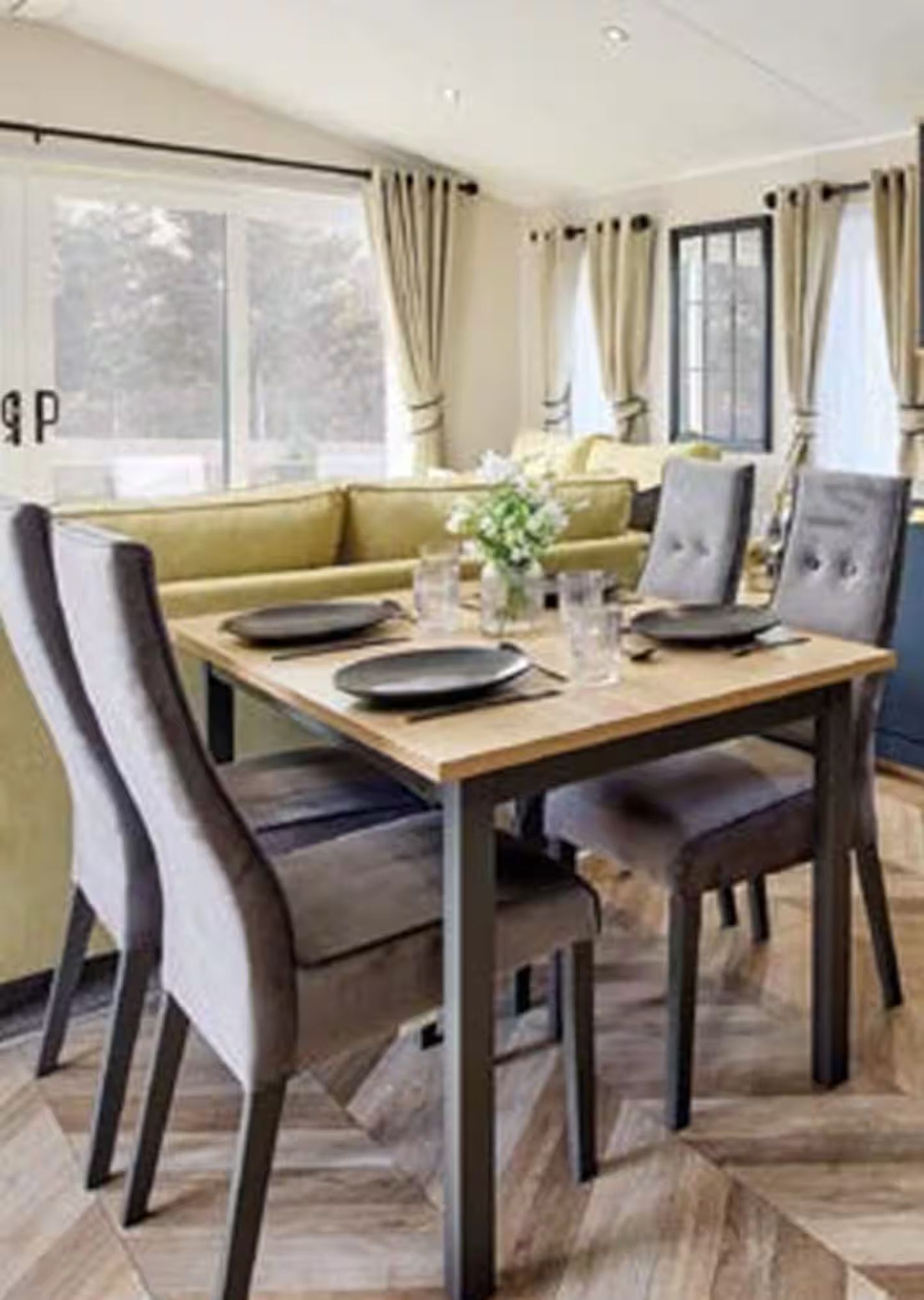 Modern dining room with a wooden table, gray chairs, and a green sectional by large windows