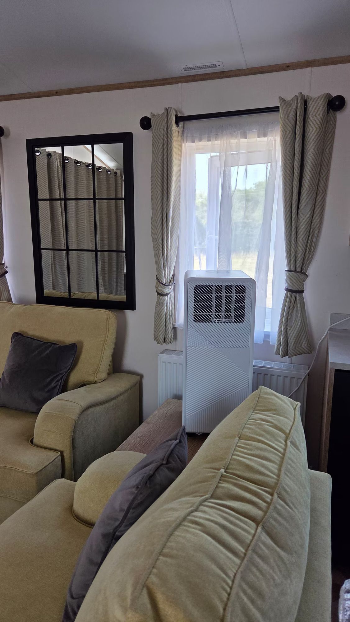 Living room with beige couches, curtained window, and portable air conditioner