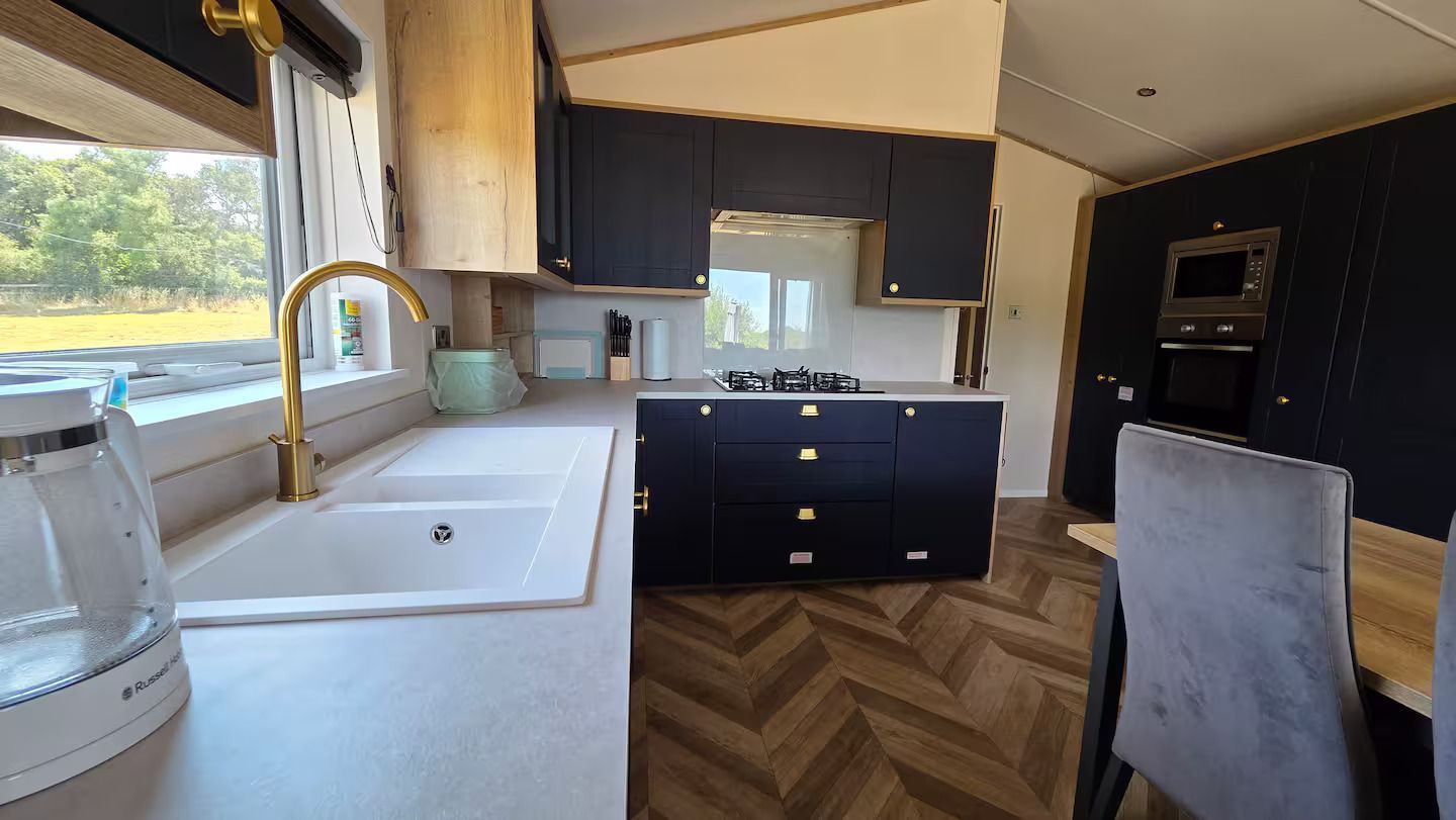 Modern kitchen interior with white sink, navy cabinets, herringbone wood floor, and large window views