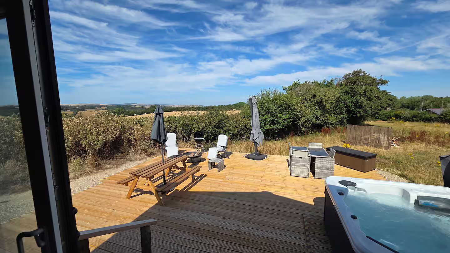 Patio with lounge chairs, umbrella, and hot tub overlooking a dry field under a blue sky