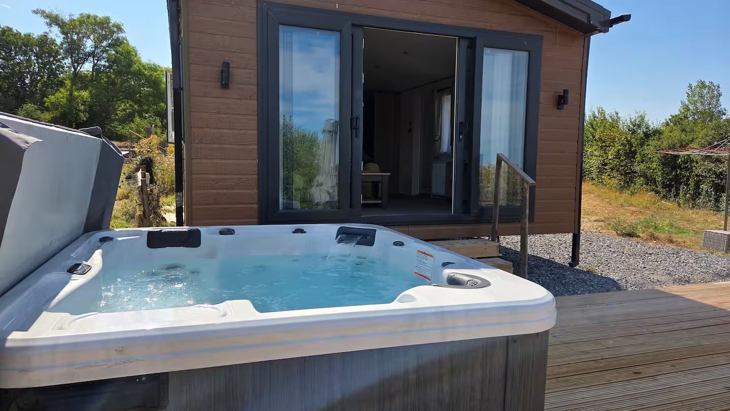 Hot tub on a wooden deck beside a modern brick house with open glass doors.
