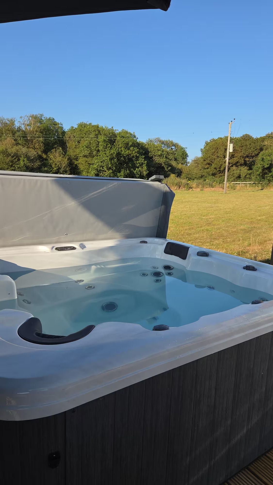 Outdoor hot tub with clear water, gray cover, and grassy yard under blue sky