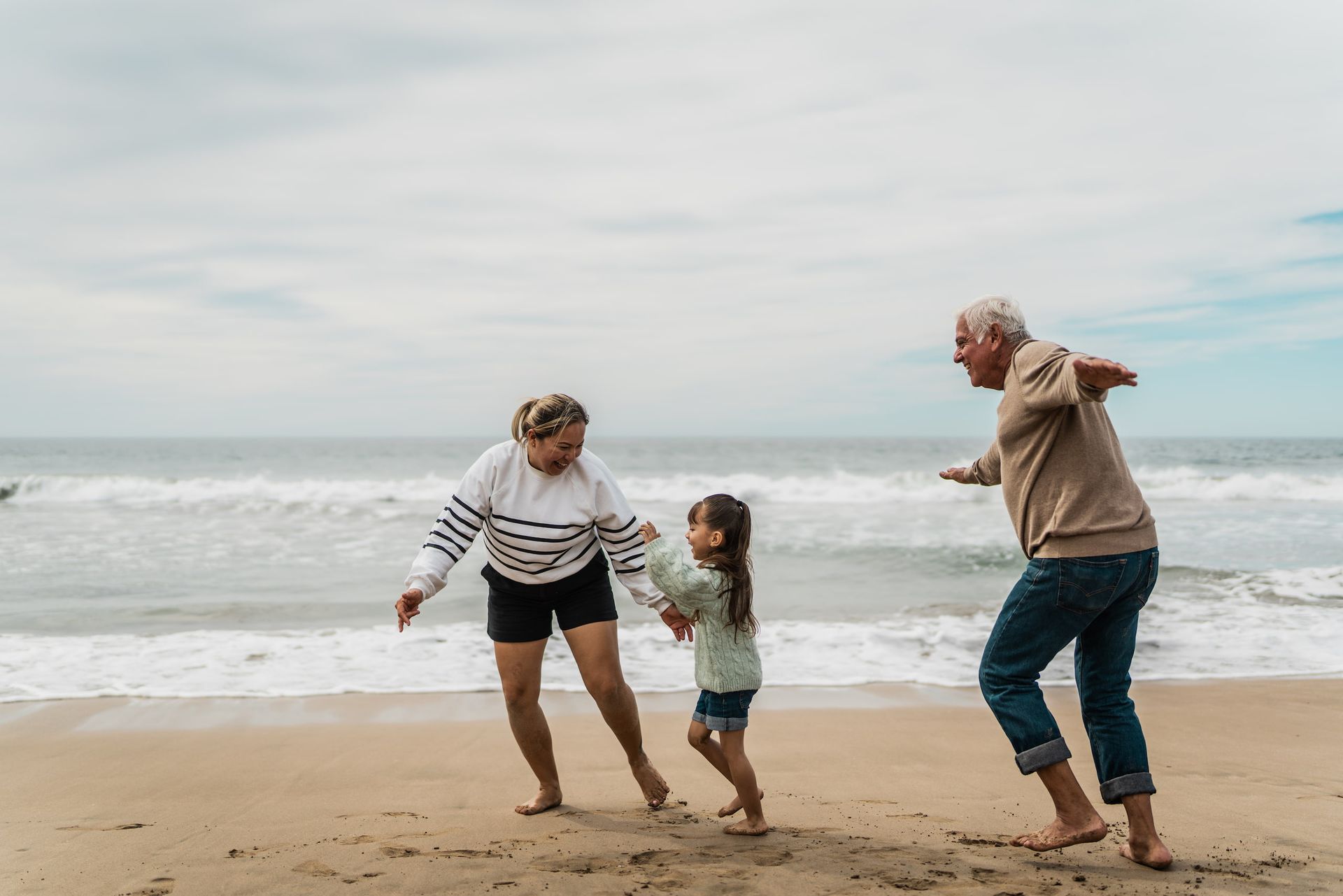 Older man kissing an older woman on the cheek; they are smiling on a beach.