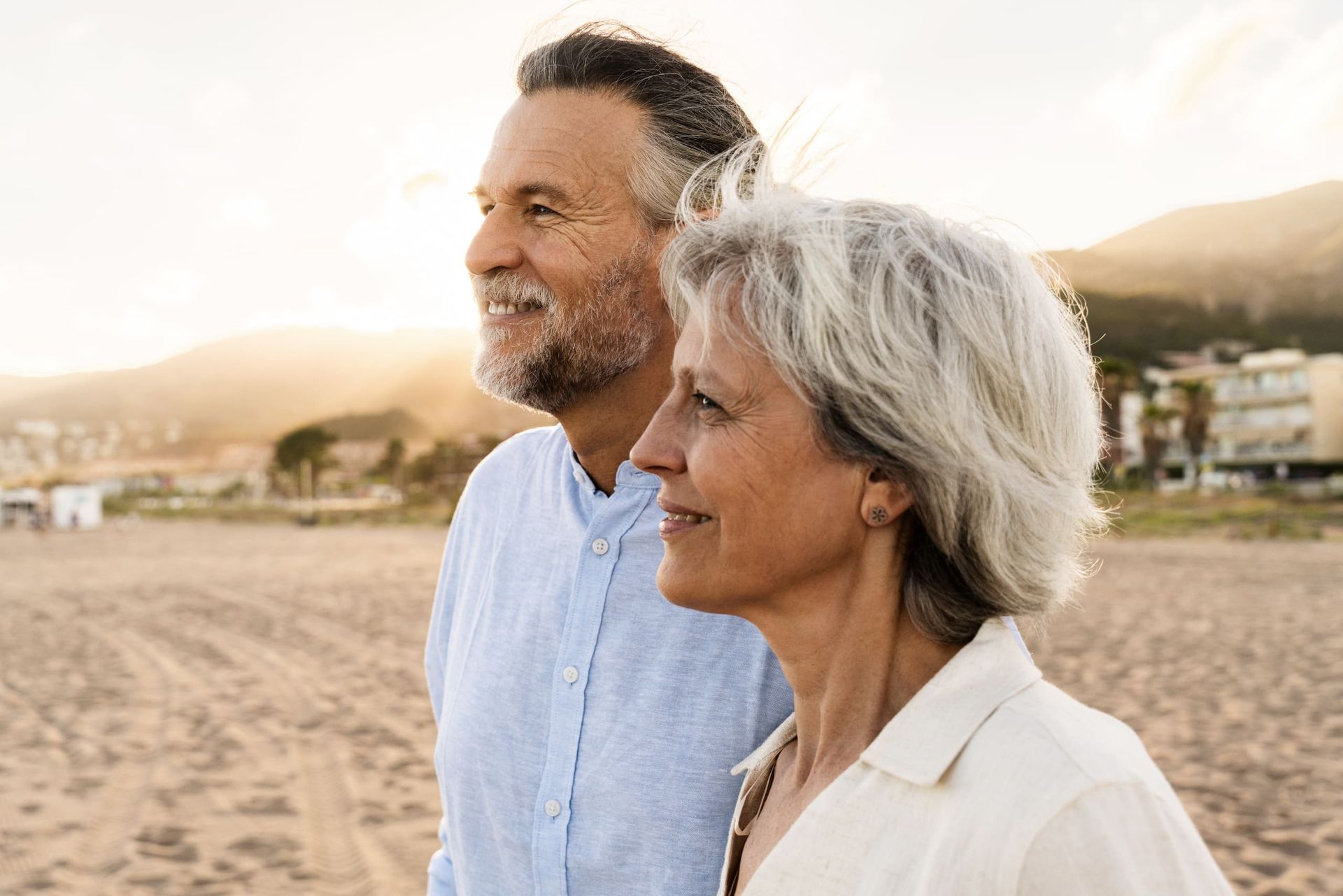 Older man kissing an older woman on the cheek; they are smiling on a beach.