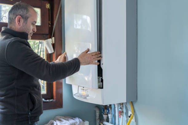 Man opening a white boiler cover on a blue wall, near a window.