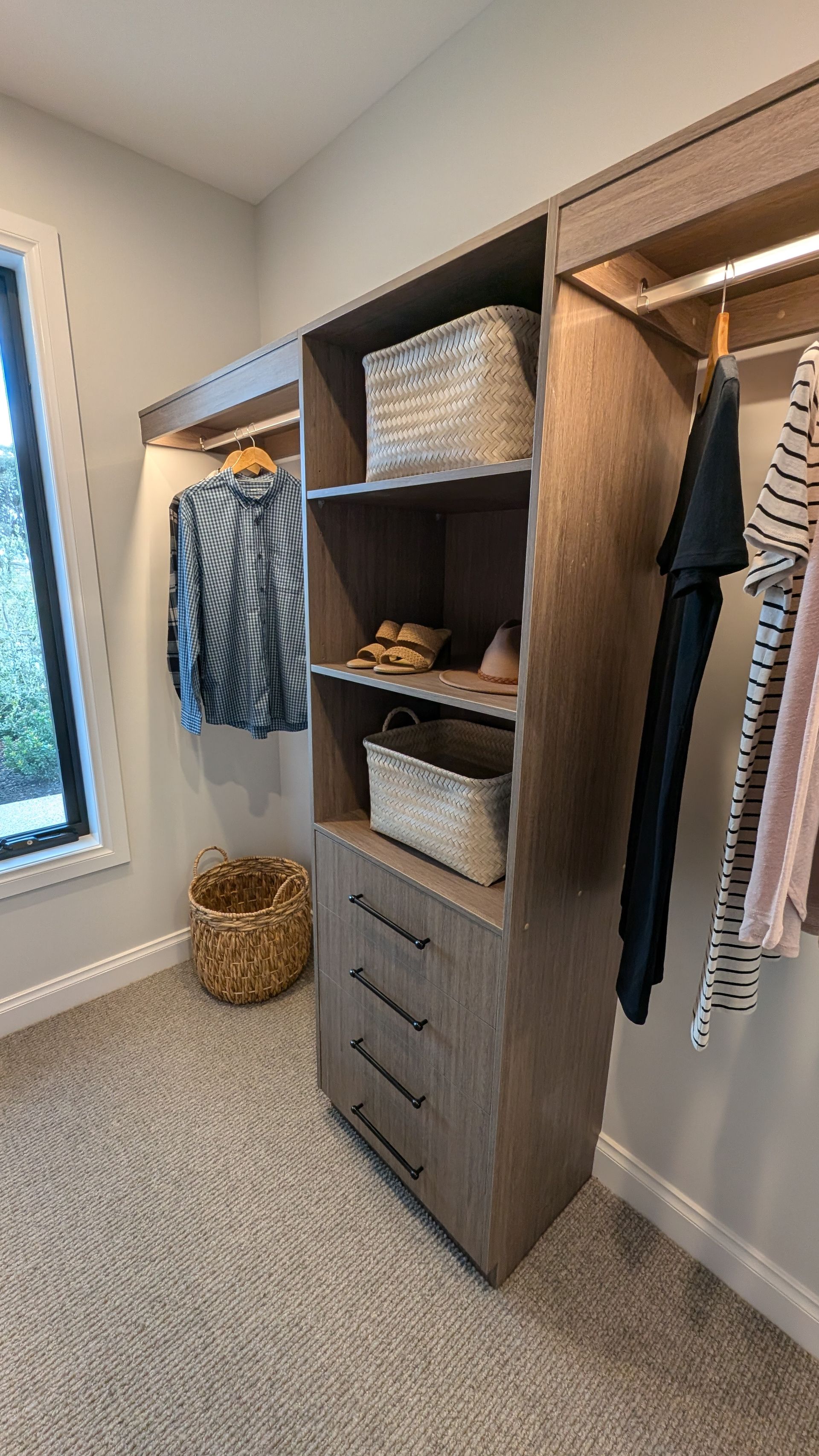 A walk in closet with clothes hanging on shelves and a window.