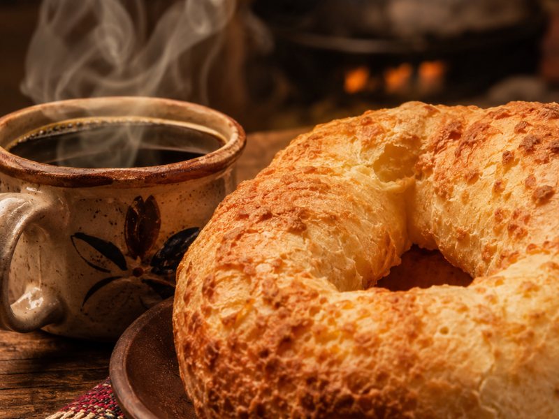 Chipa assada servida ao lado de uma xícara de café quente com fumaça.