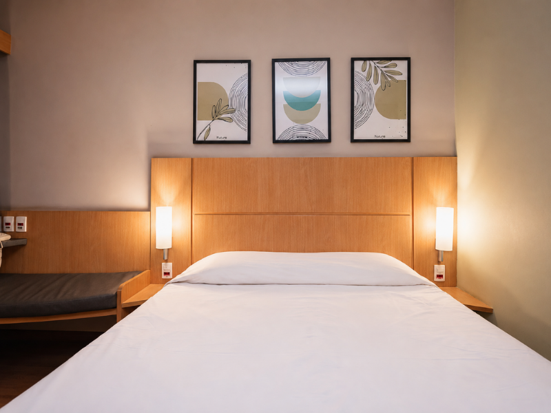 Quarto aconchegante com cama de casal, iluminação suave e decoração moderna no Hus Hotel Dourados.