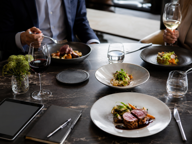 Jantar de negócios em restaurante sofisticado de Maringá com pratos gourmet, taças de vinho, tablet e agenda sobre a mesa, ideal para reuniões executivas.