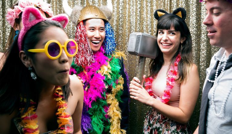 Four people in colorful costumes and party accessories posing in front of a gold tinsel backdrop