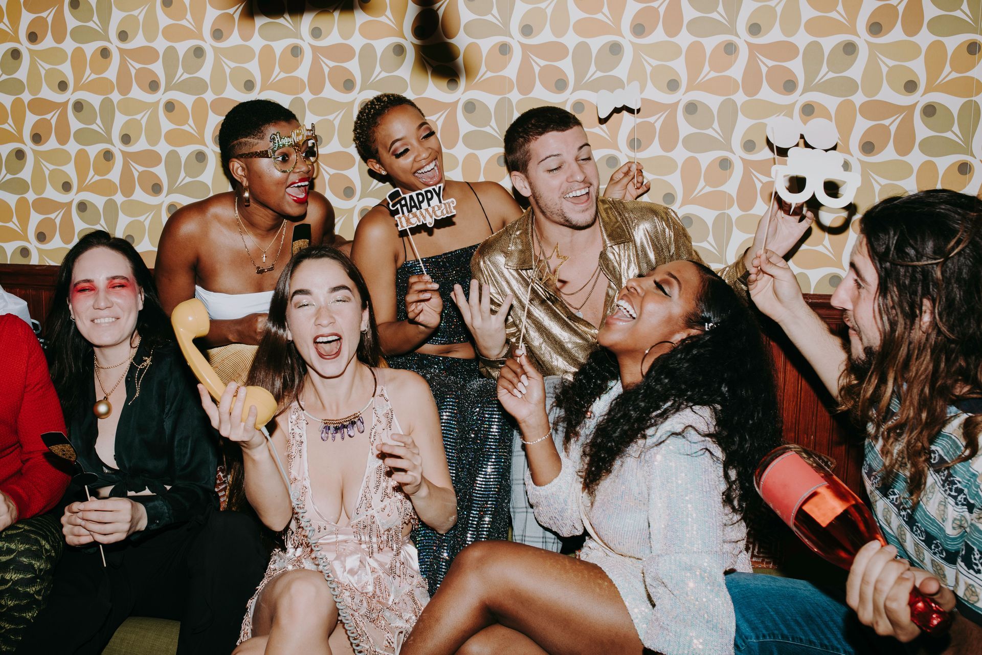 Friends celebrating at a party, smiling and posing with gold balloons against patterned wallpaper.