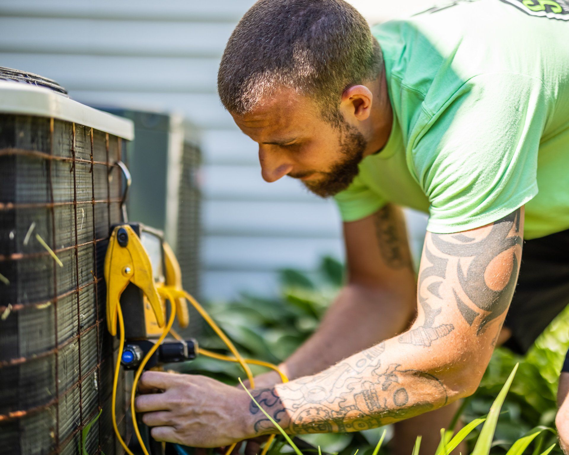 HVAC technician checks AC unit with gauges outdoors; wearing green shirt.