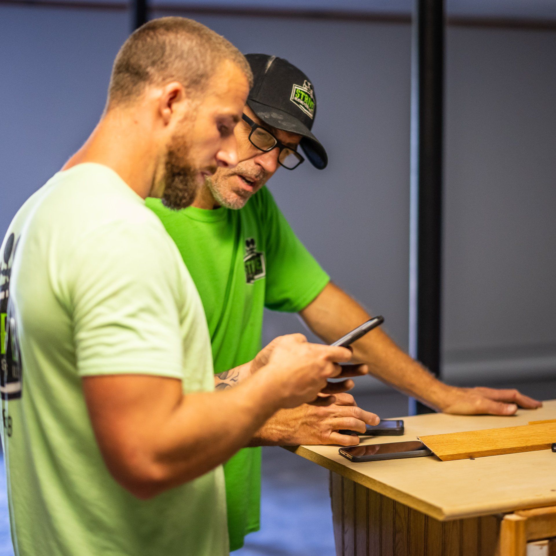 Two men looking at a phone together, possibly working on a project; one in green shirt.
