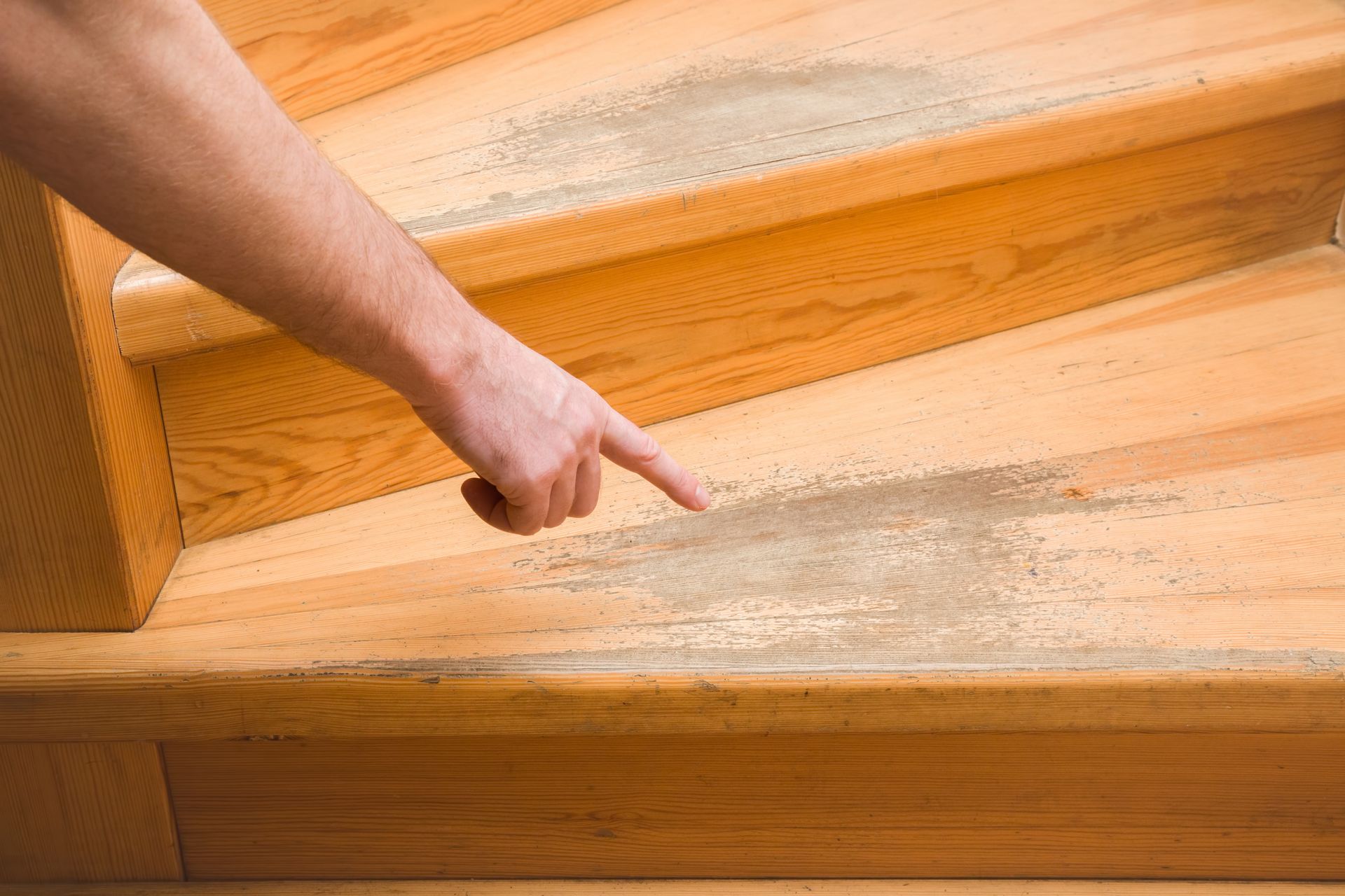 Une main pointant du doigt vers une planche de bois endommagée parmi d'autres planches de parquet.