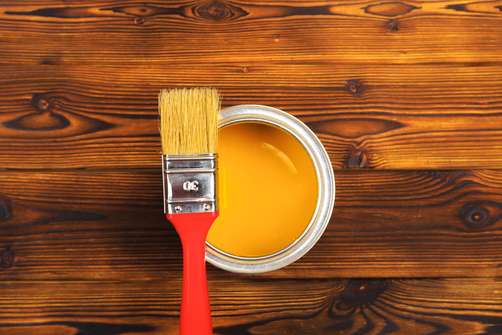 Un pinceau rouge posé sur une surface en bois, dans un pot de peinture jaune-orange ouvert.