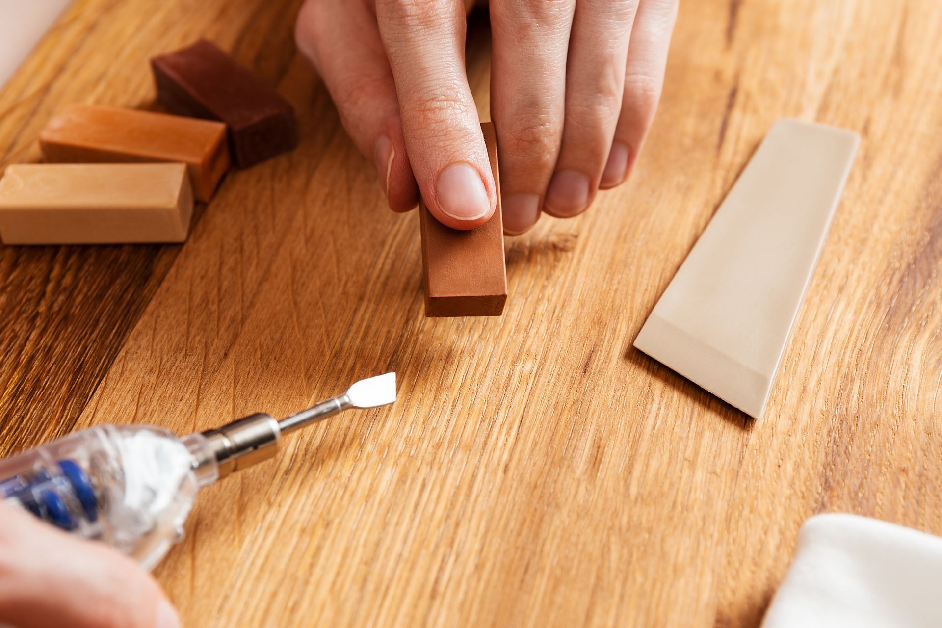 Des mains ponçant un petit bloc de bois sur un établi, des outils à proximité