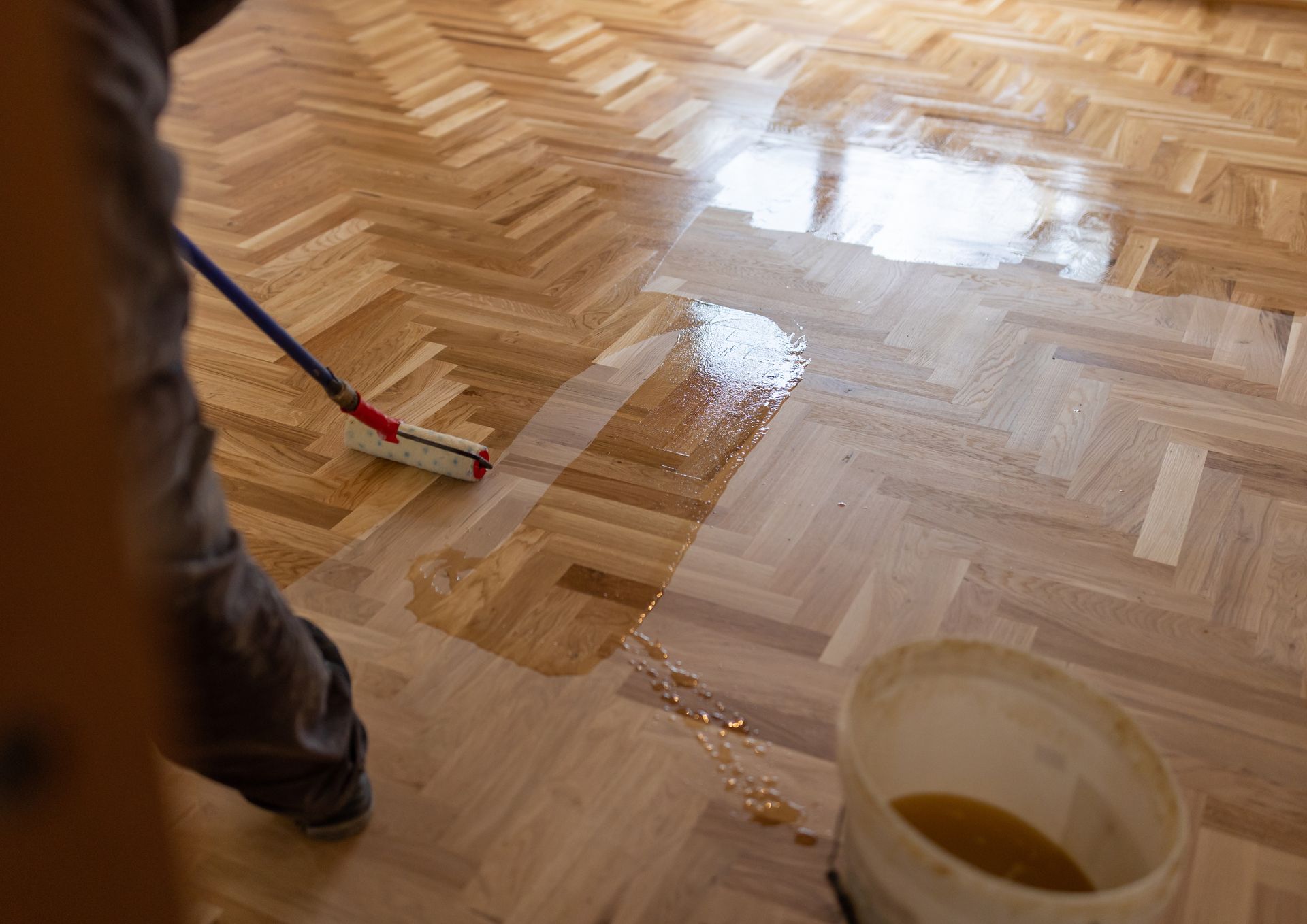 Une personne lave un parquet mouillé avec une serpillière rouge et bleue ; un seau est visible au premier plan.