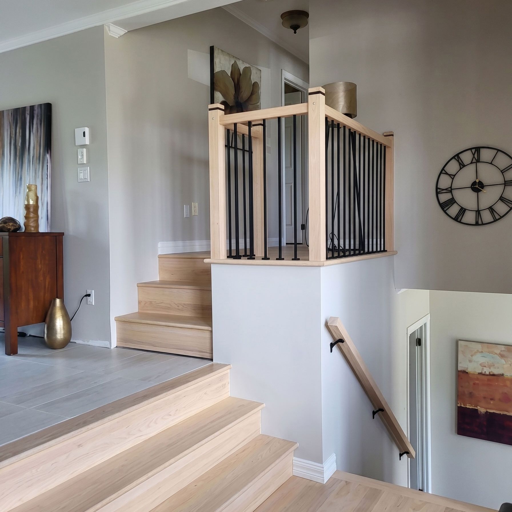 Escalier intérieur avec marches en bois clair, rampes noires et horloge murale dans une maison moderne.