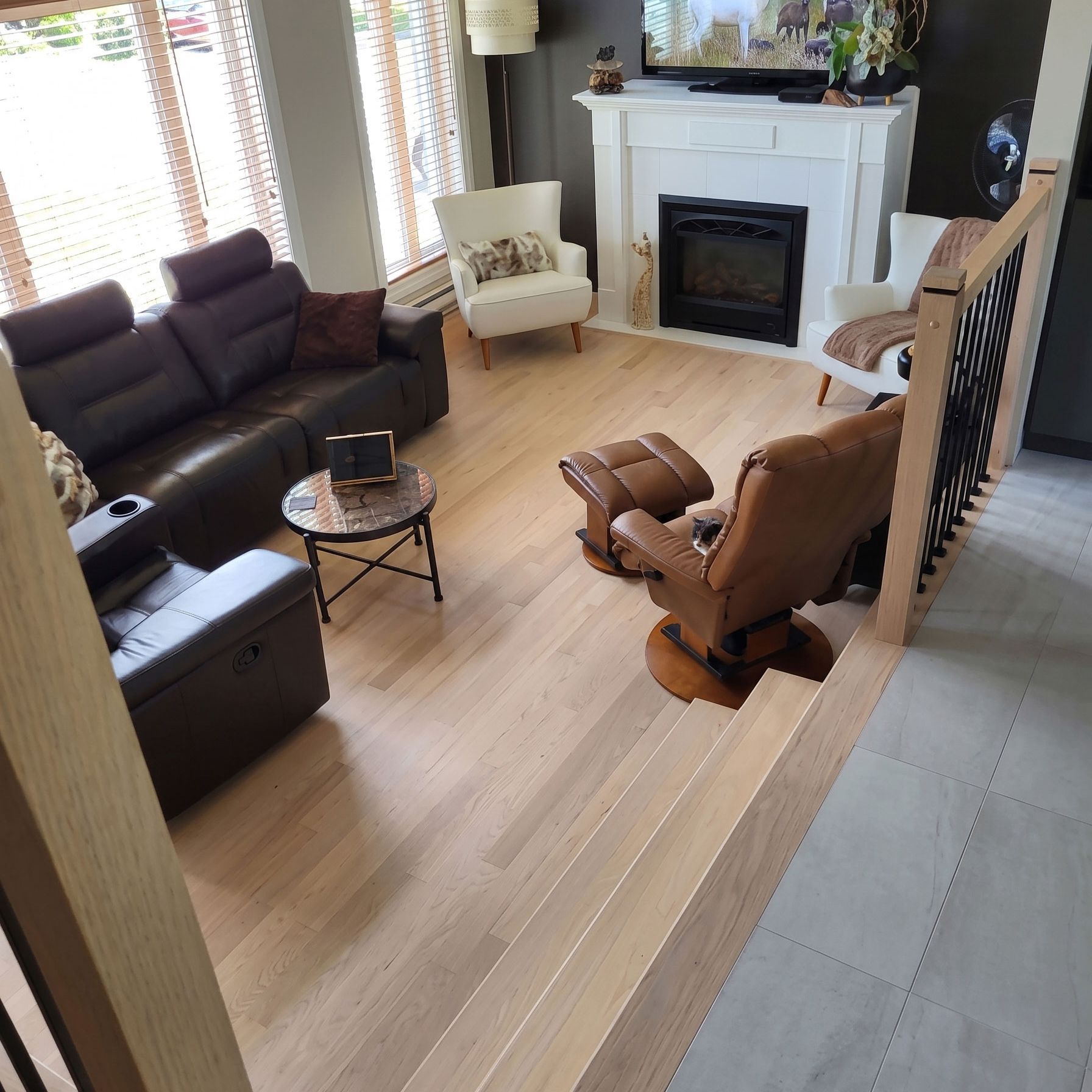 Salon confortable avec canapé d'angle marron, cheminée, fauteuil à bascule et parquet clair