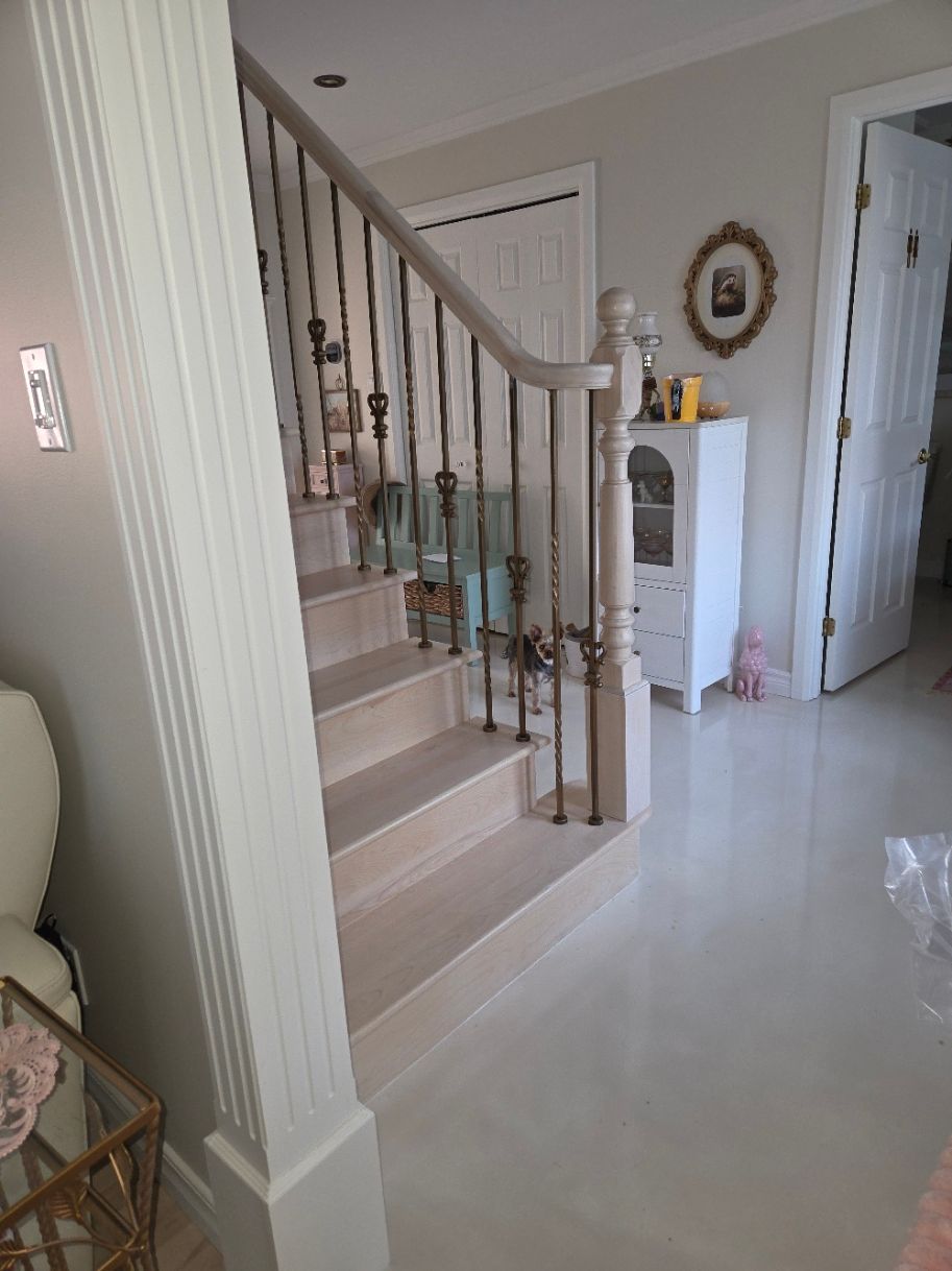 Hall d'entrée lumineux avec escalier, sol blanc brillant et petit meuble près d'un miroir.