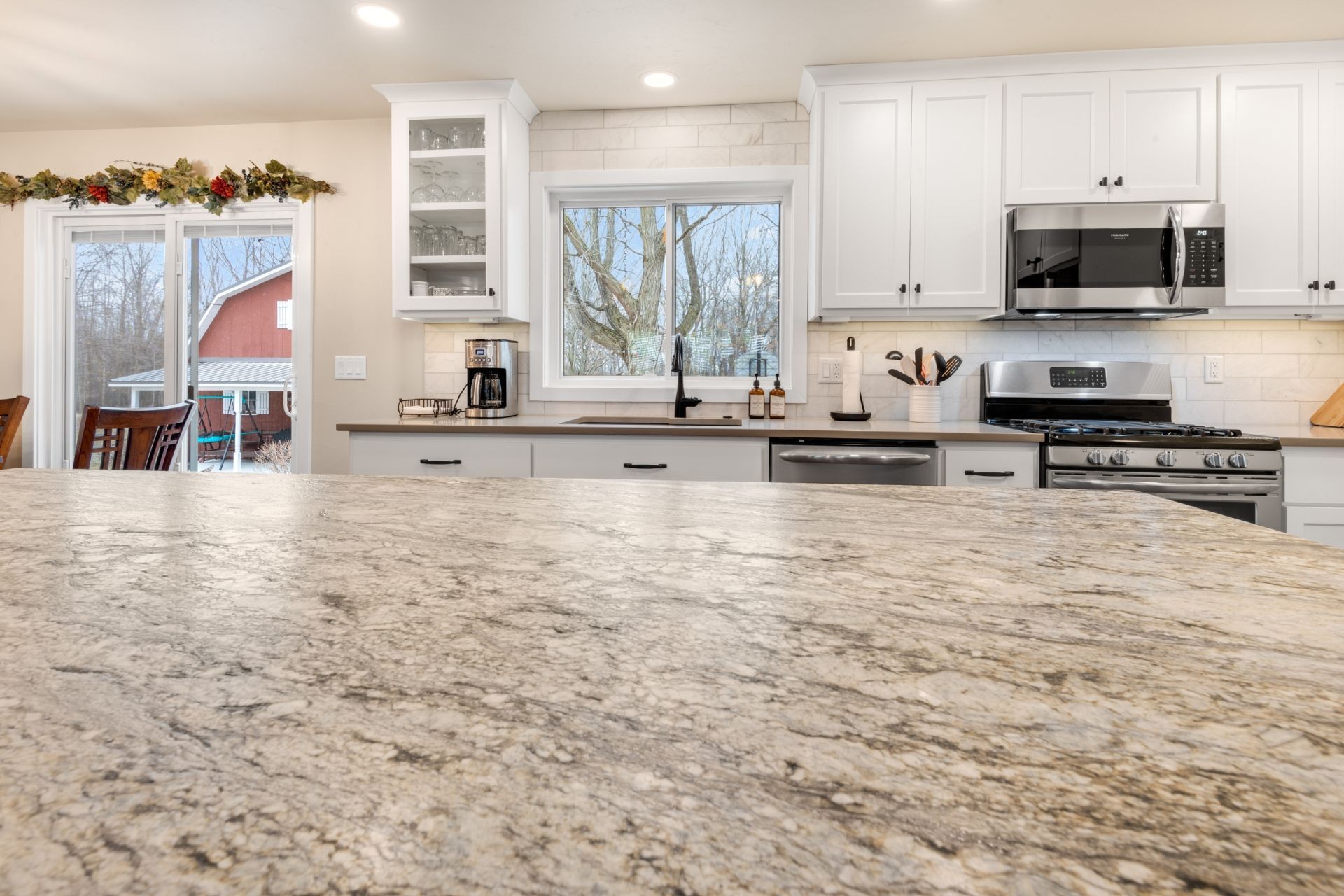 A kitchen with granite counter tops , white cabinets , stainless steel appliances and a large window.