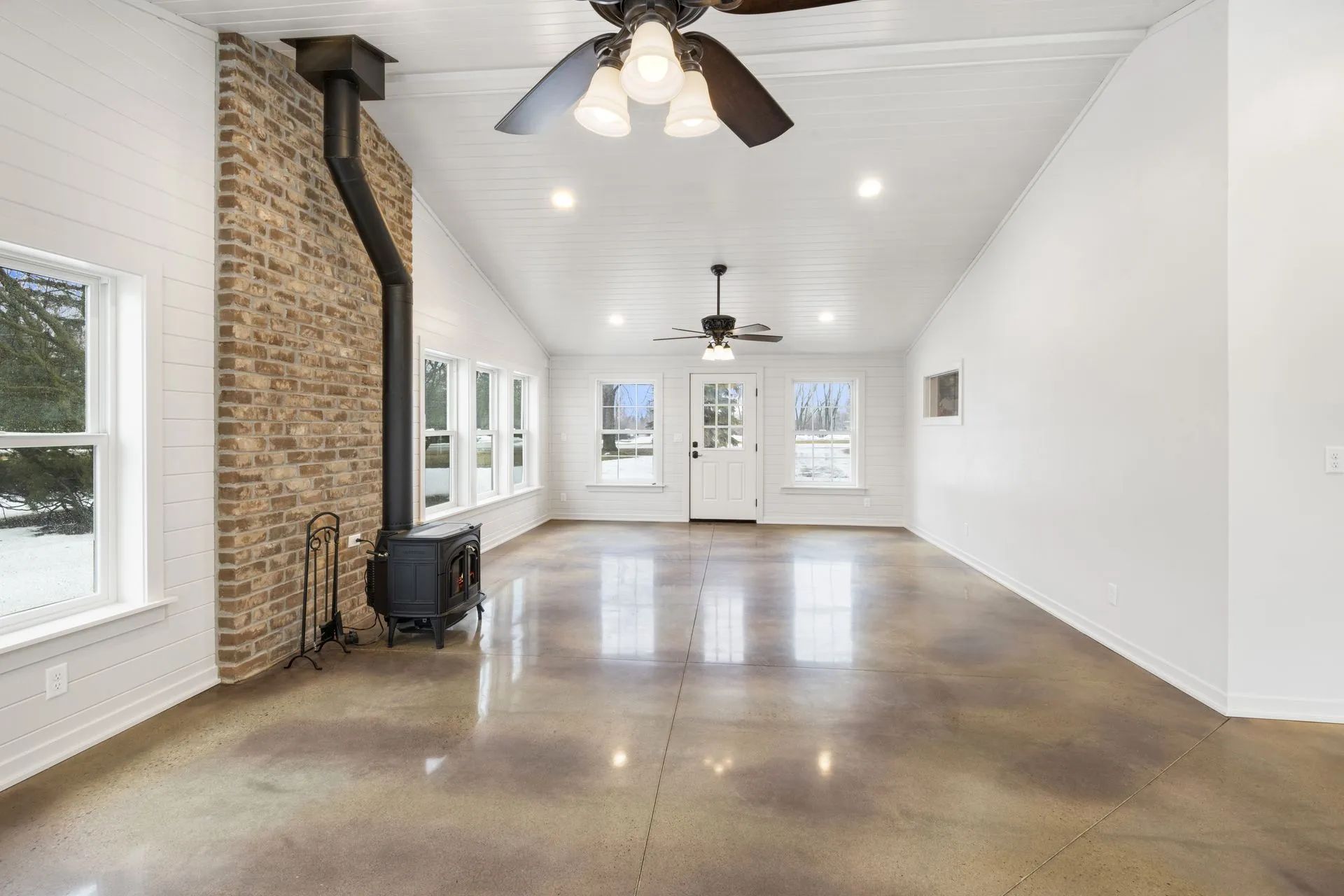 A large empty room with a ceiling fan and a wood stove.