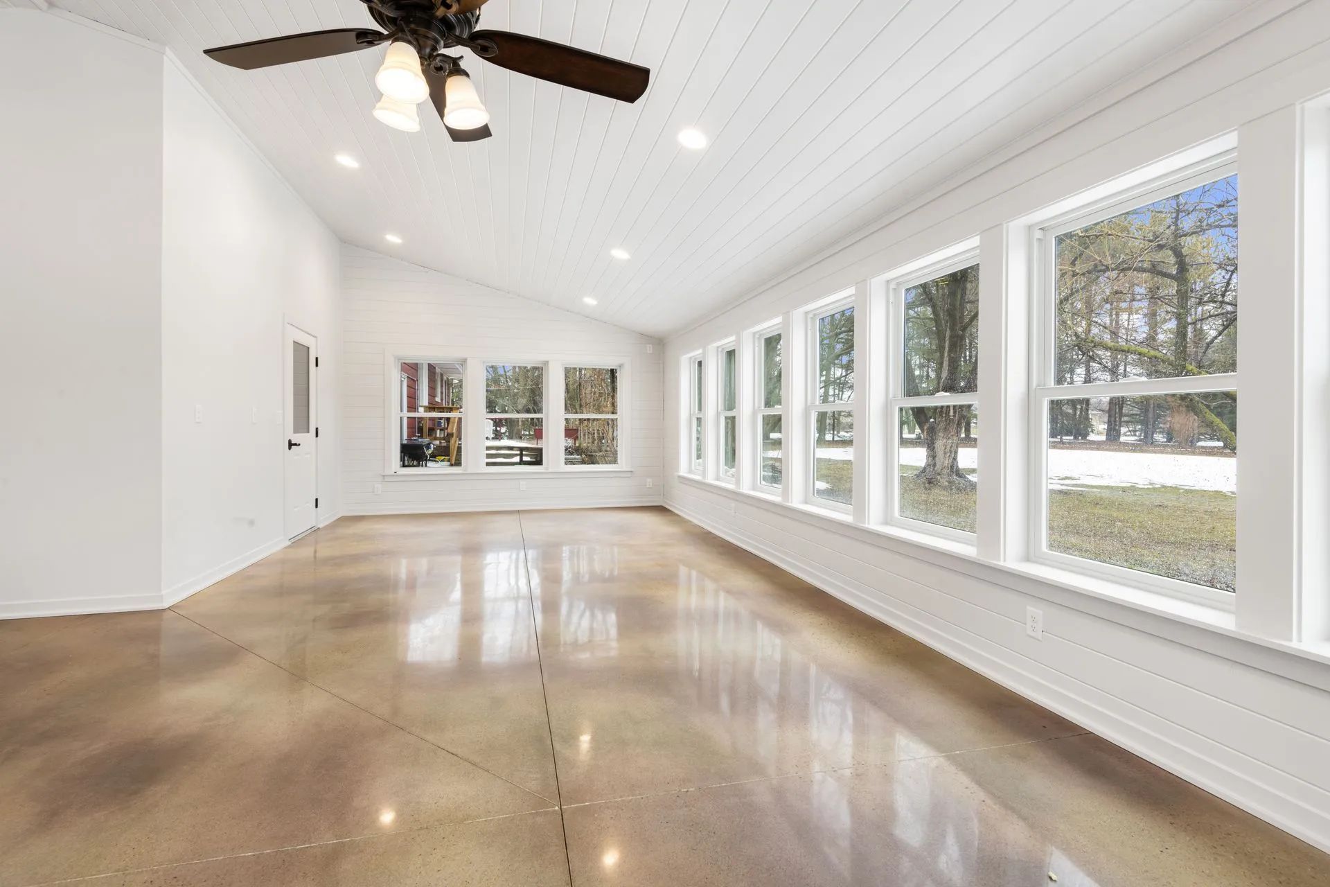 A large empty room with a lot of windows and a ceiling fan.