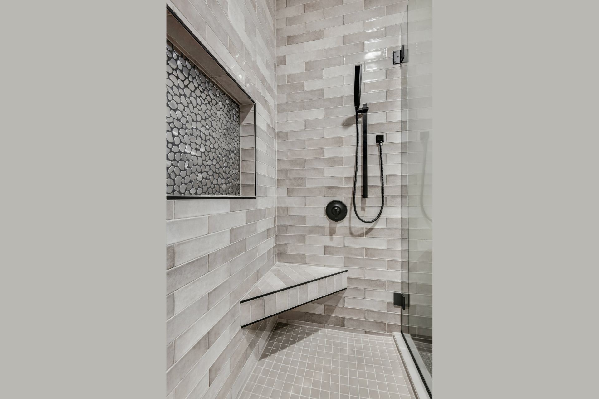 Modern tiled shower with black fixtures, built-in bench, and frosted window.