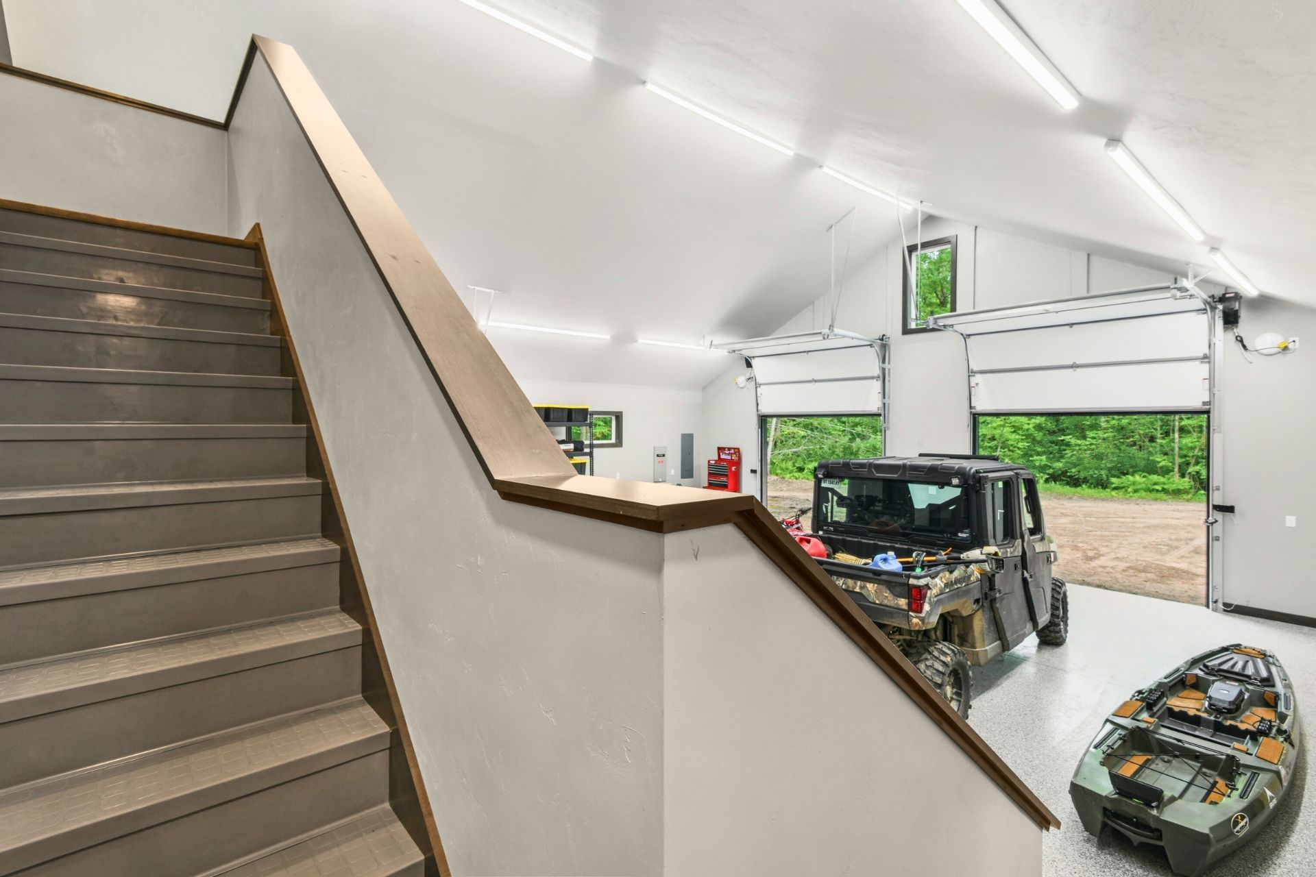 Staircase overlooking a bright garage with an SUV and an open rolling door