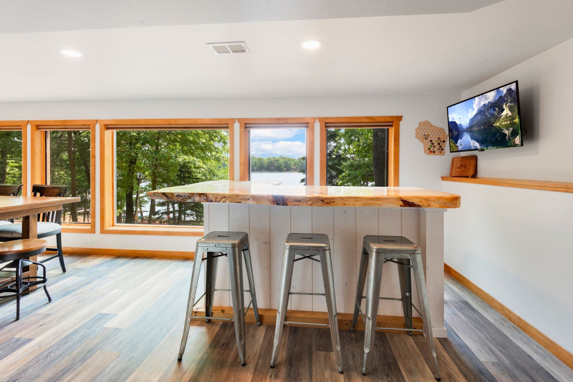 A living room with a table and stools and a television on the wall.