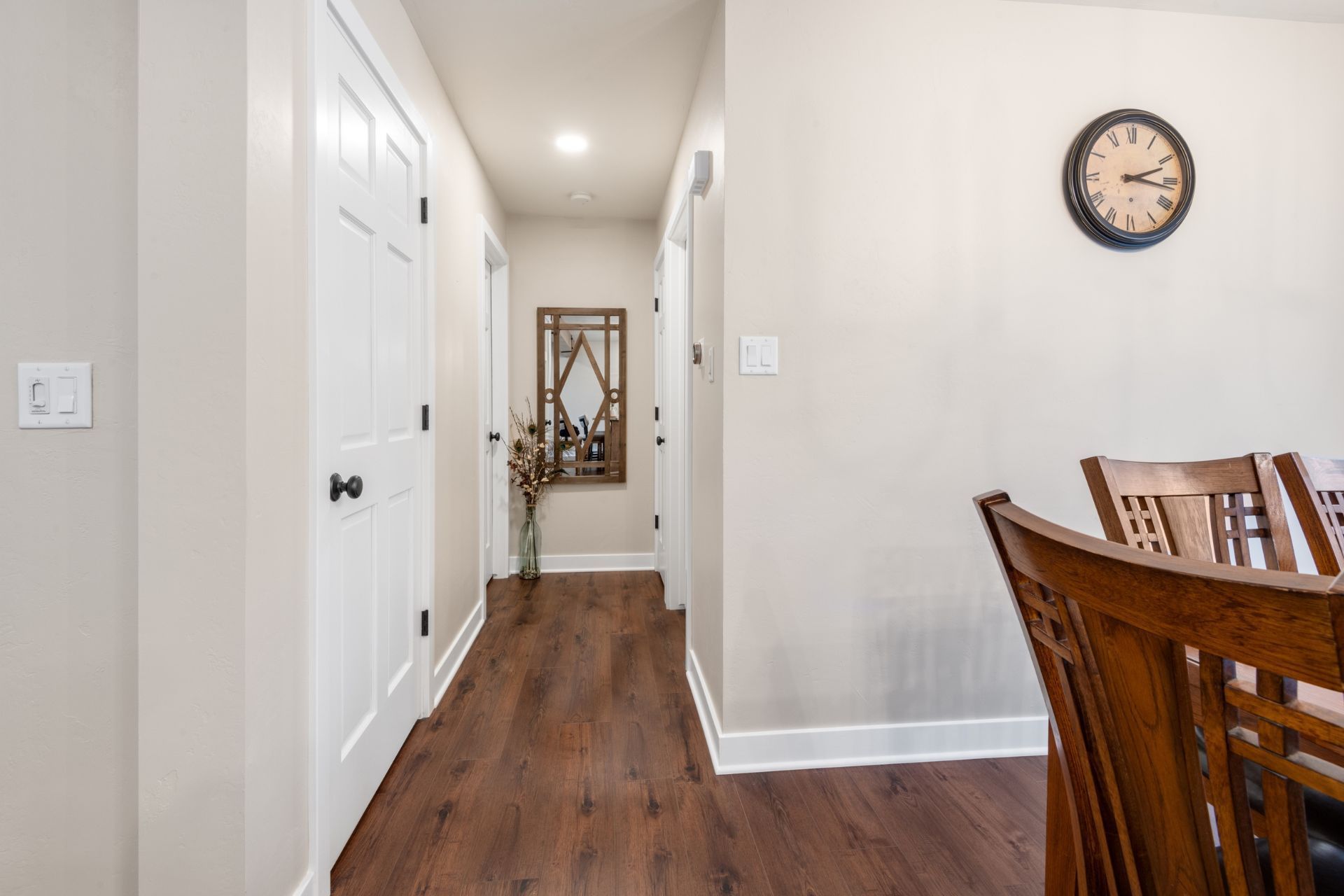 A hallway leading to a dining room with a clock on the wall.
