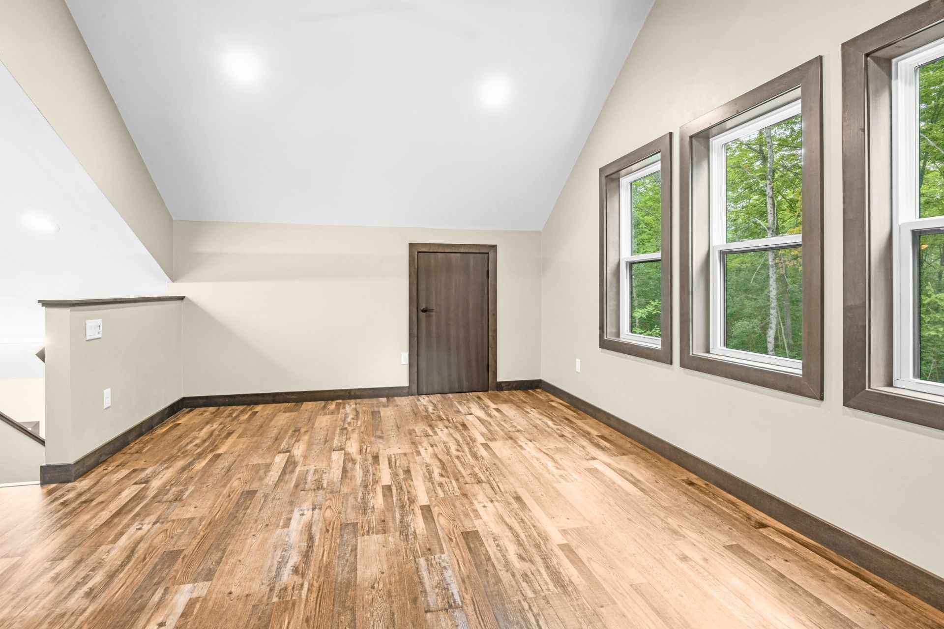 Empty room with hardwood floors, sloped ceiling, and three windows along the right wall.