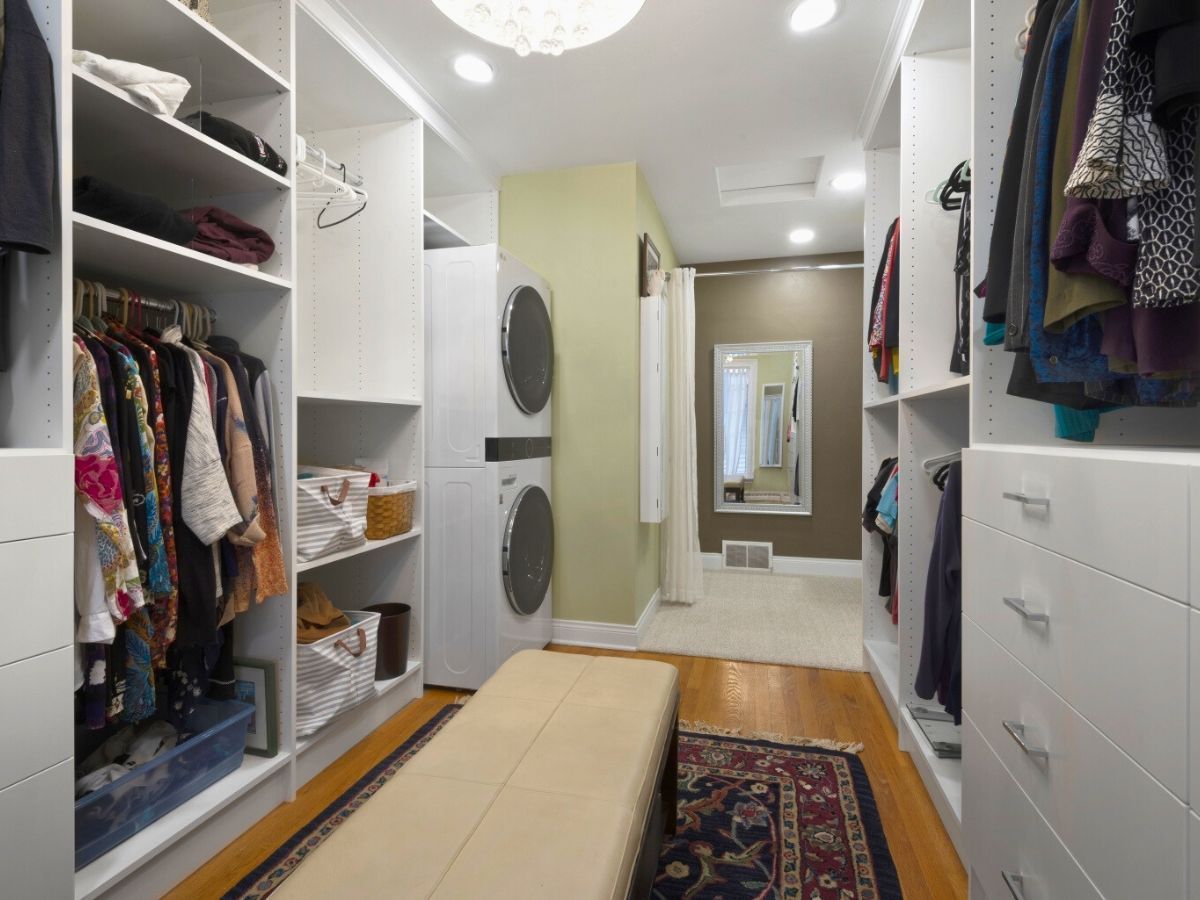 A walk in closet with a bench and a washer and dryer