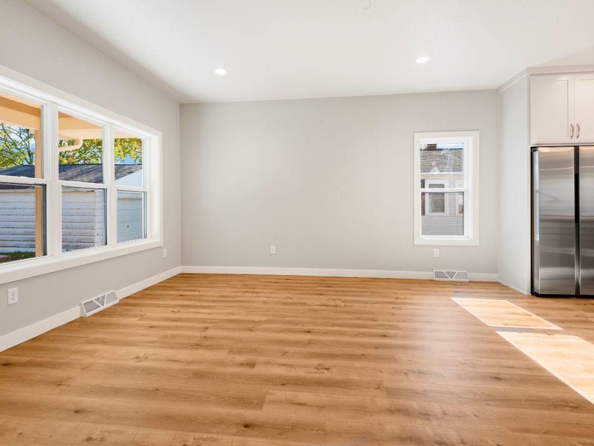 An empty living room with hardwood floors and a refrigerator.