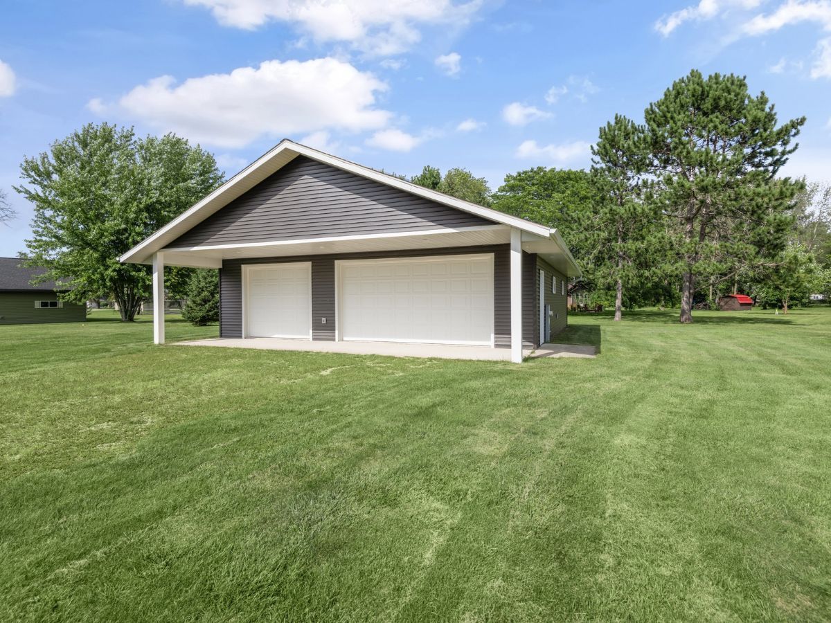 A garage with a covered porch is in the middle of a lush green field.
