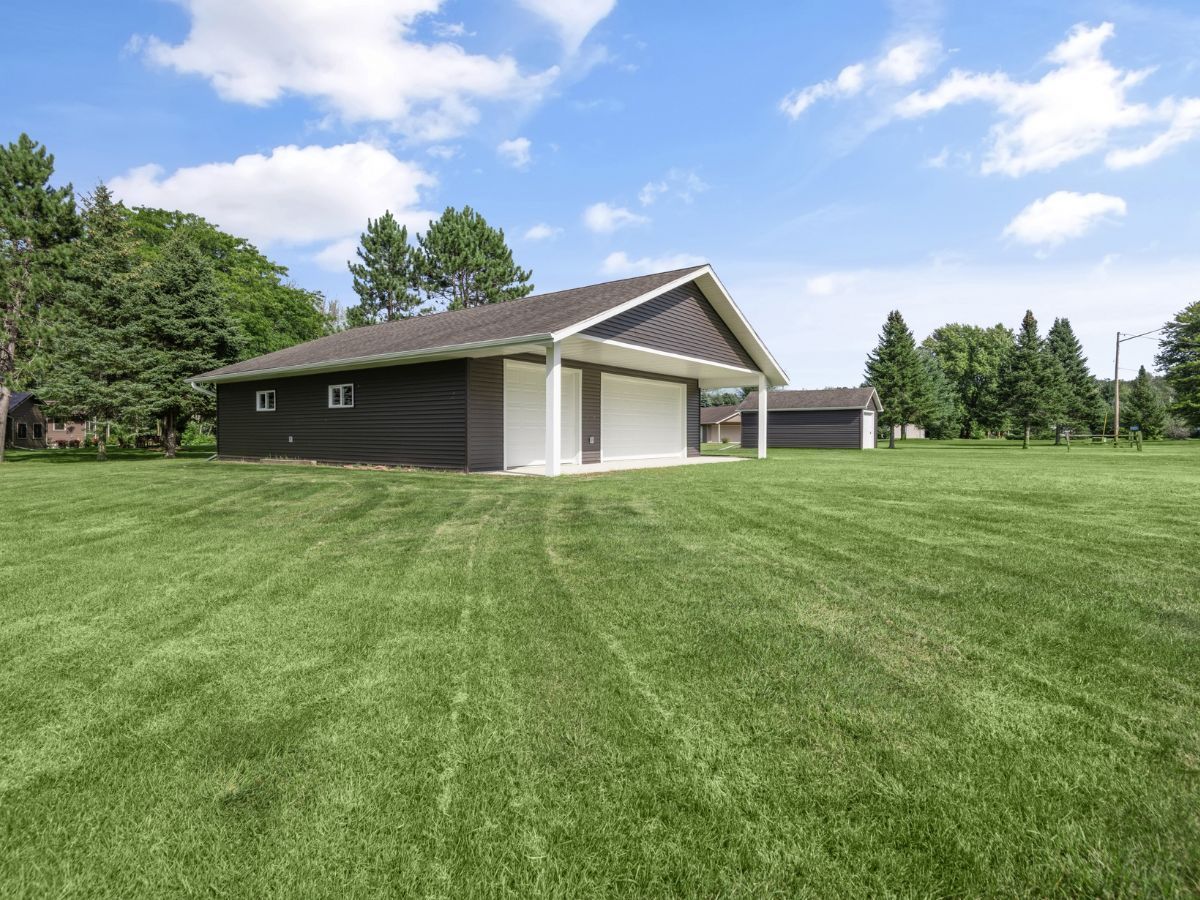 A black garage with a white door is in the middle of a lush green field.