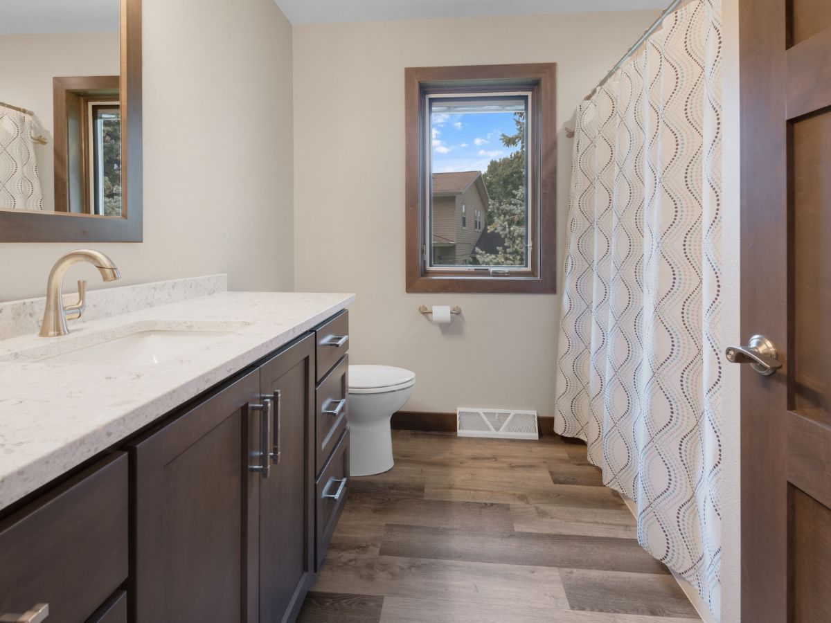 A bathroom with a toilet , sink , mirror and shower curtain.