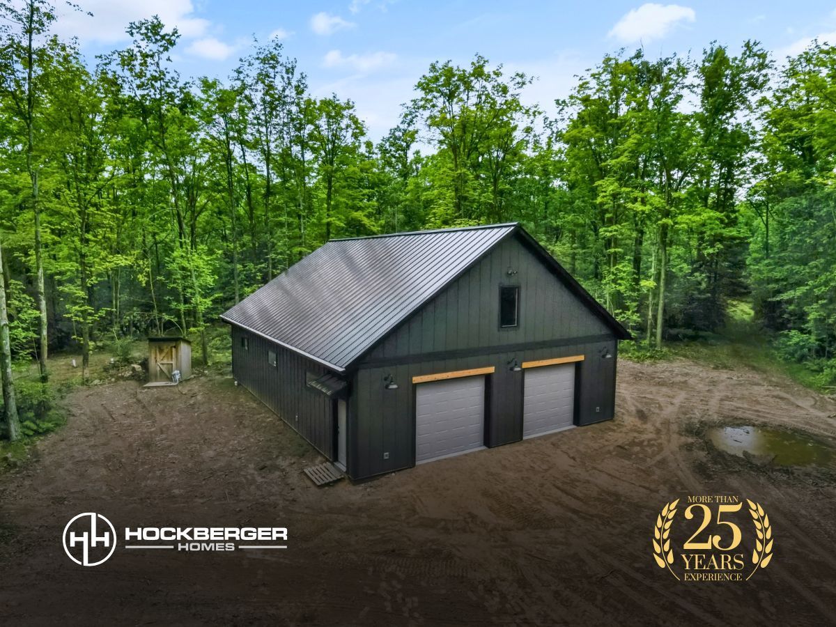 Dark gray two-bay barndominium with metal roof in a wooded yard, aerial view