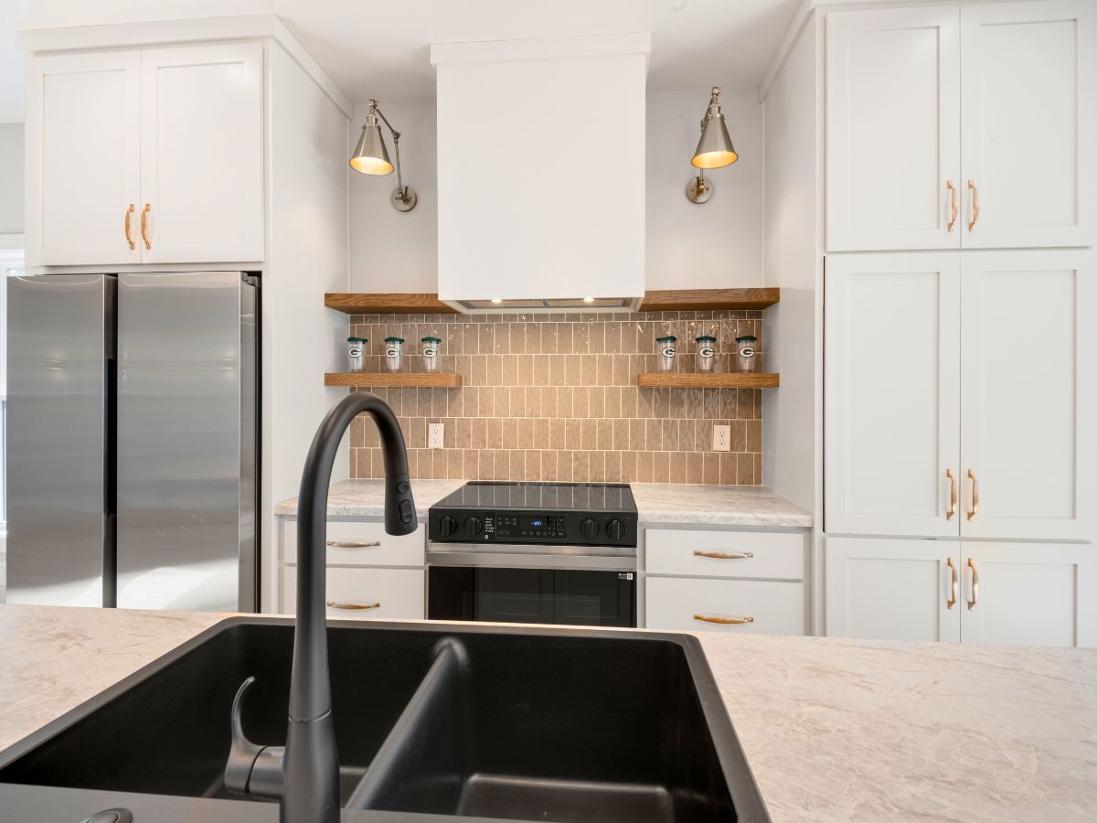 A kitchen with white cabinets , a black sink , a stove , and a refrigerator.