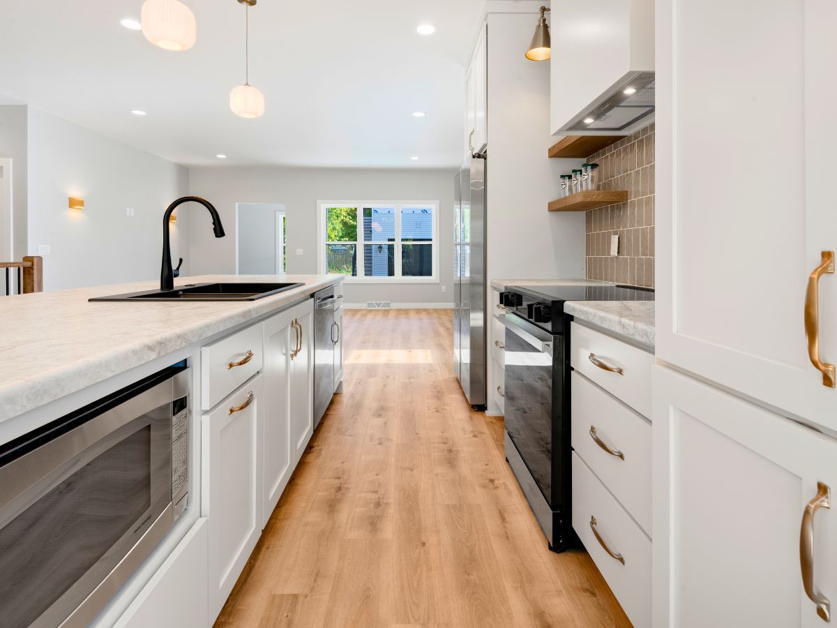 A kitchen with white cabinets , stainless steel appliances , wooden floors and a sink.