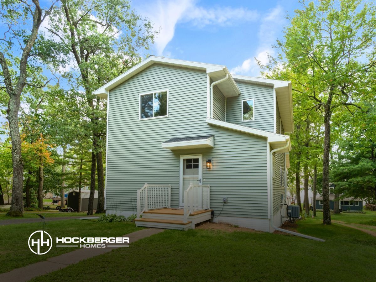 A house with a green siding is surrounded by trees