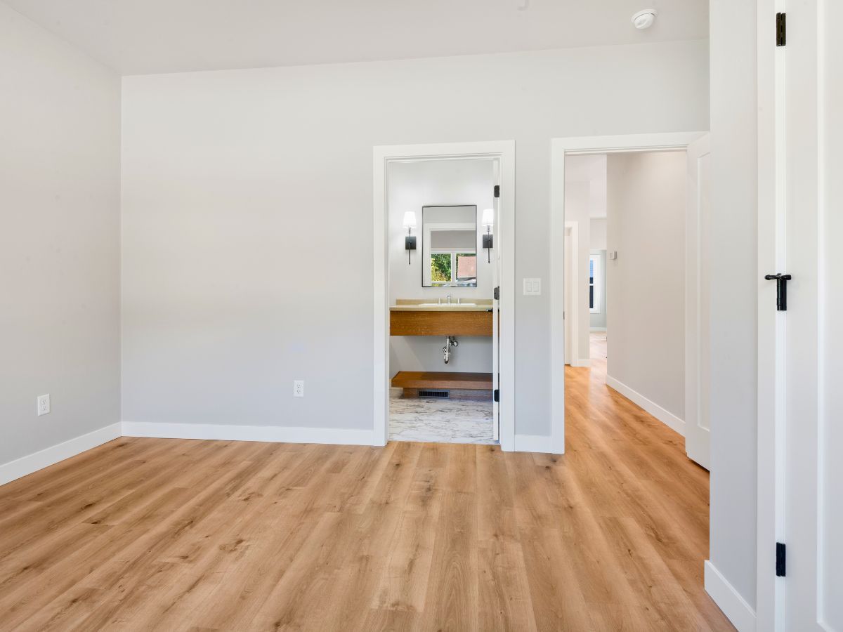 An empty room with hardwood floors and a bathroom in the background