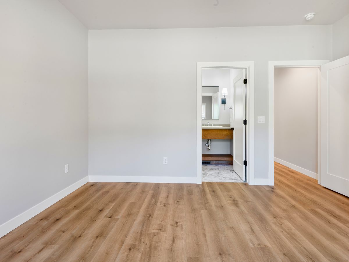 An empty room with hardwood floors and a bathroom in the background.