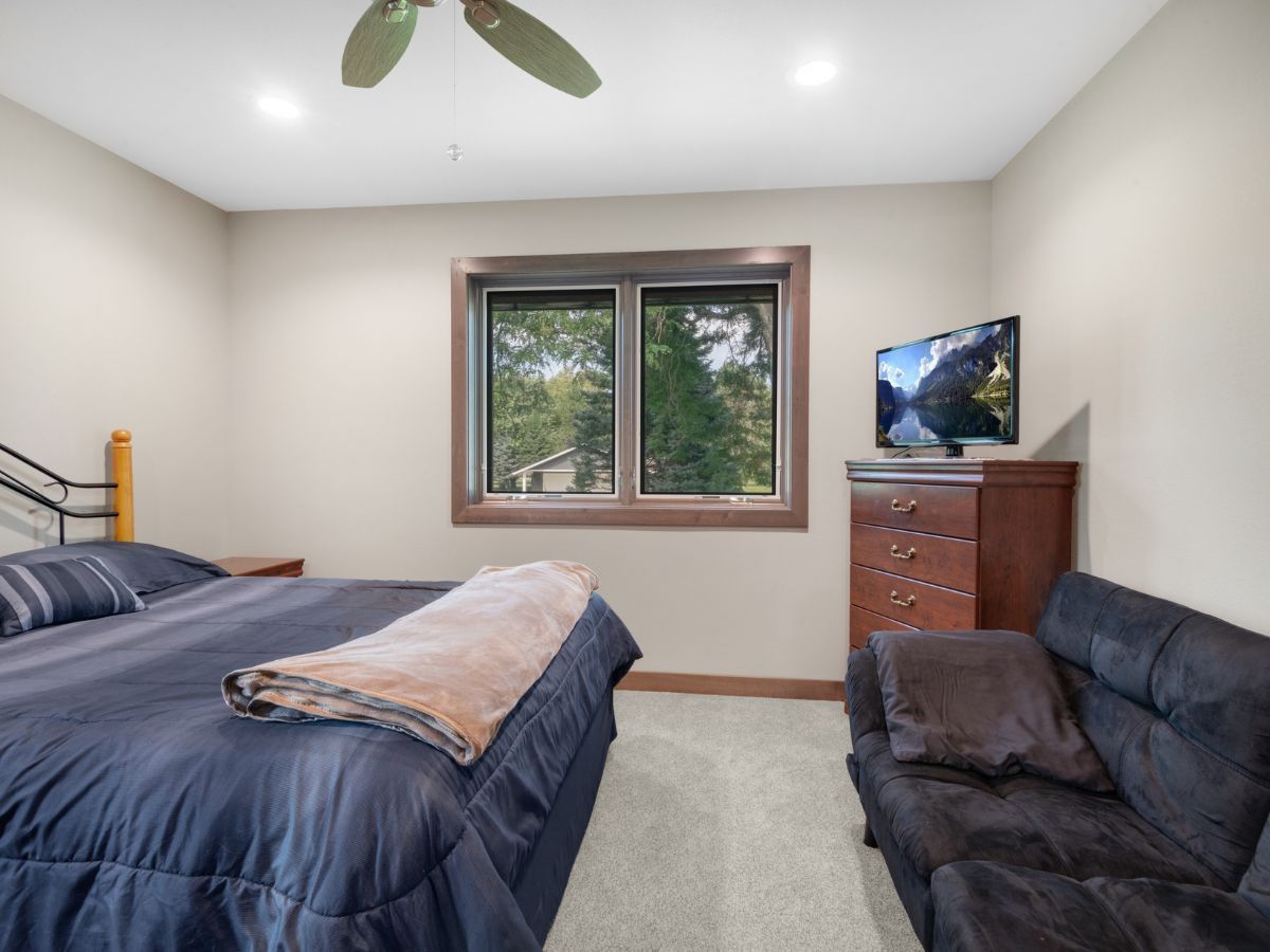 A bedroom with a bed , couch , television and ceiling fan.