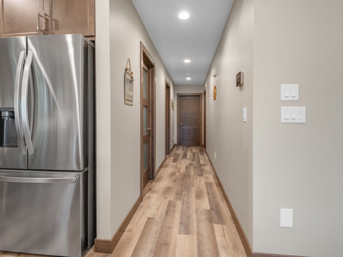 A long hallway with hardwood floors and a stainless steel refrigerator