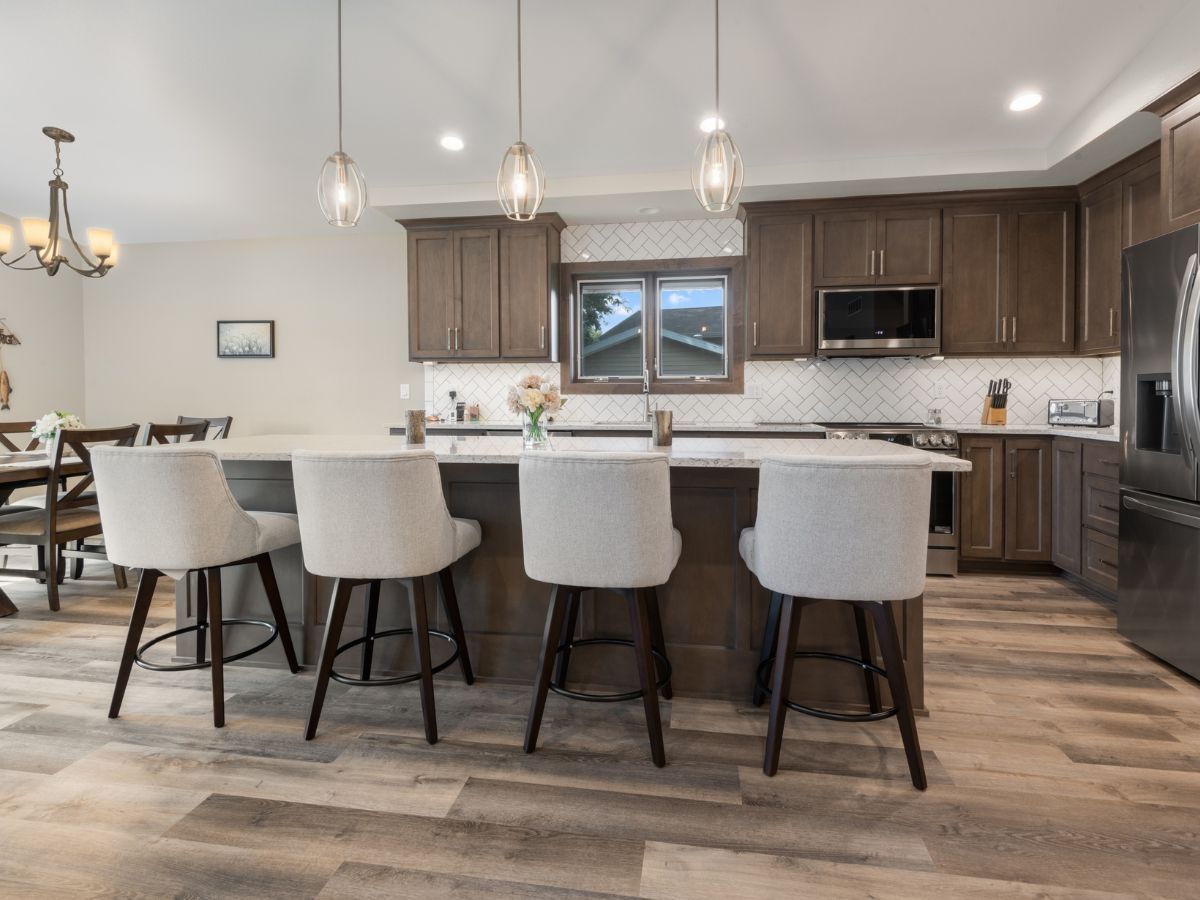 A kitchen with a large island , stools , and a refrigerator.