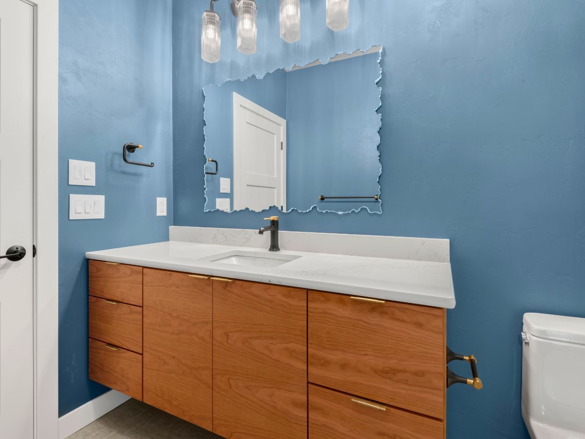 A bathroom with blue walls , a sink , a toilet and a mirror.