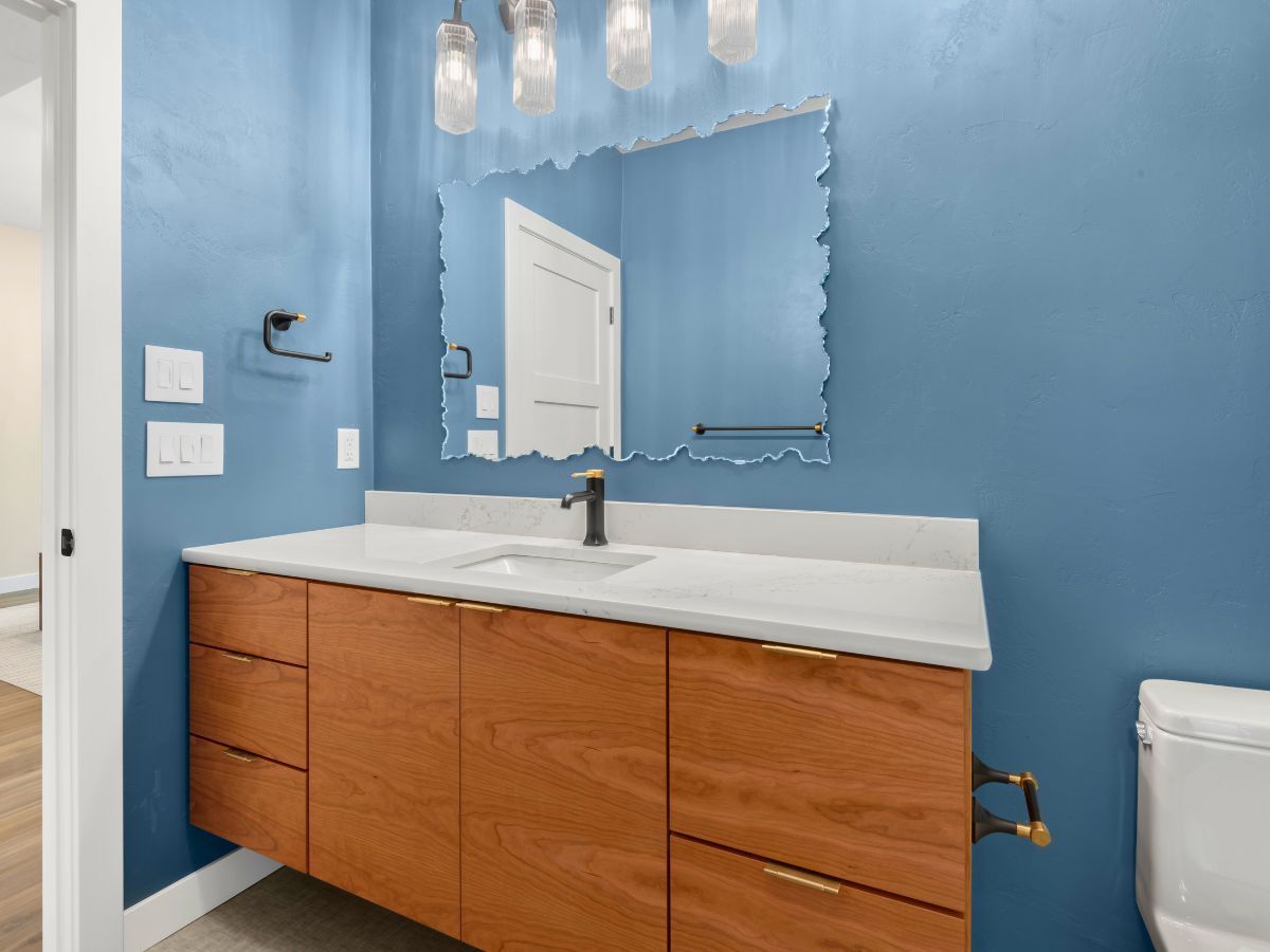 A bathroom with blue walls , a sink , a mirror and a toilet.