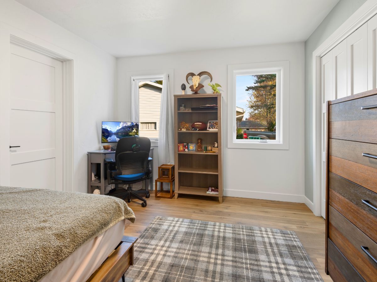 A bedroom with a bed , dresser , desk , chair and window.